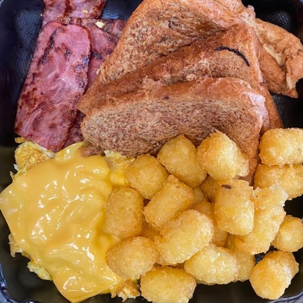 A breakfast platter with grilled ham, scrambled eggs with melted cheese, tater tots, and toast.