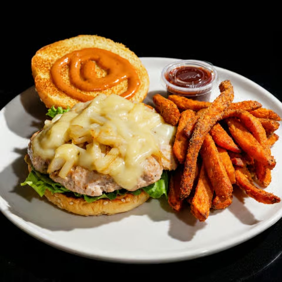 Cheeseburger with melted cheese and caramelized onions, sweet potato fries, and a side of barbecue sauce.