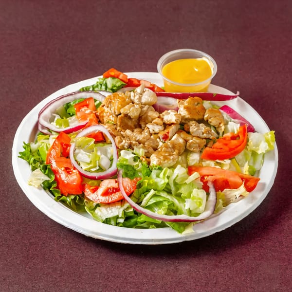Chicken salad with lettuce, tomatoes, red onions, and a side of dressing.