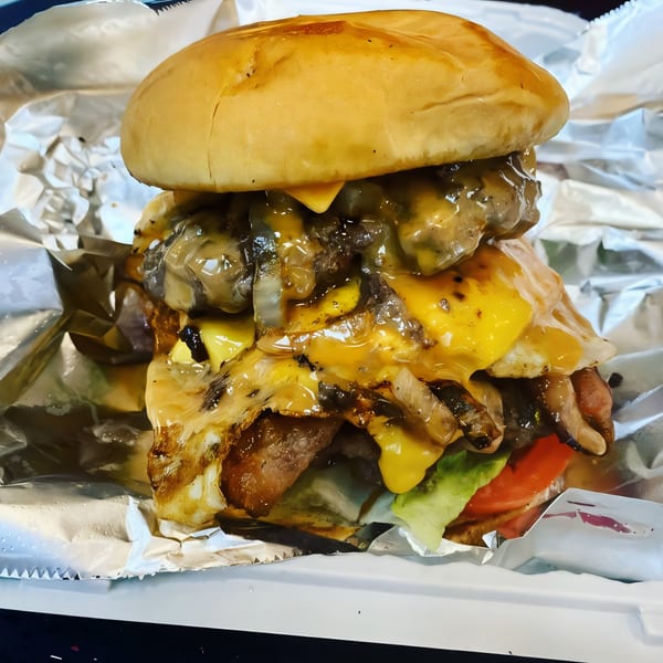 A Go To Burger with melted cheese, mushrooms, onions, bacon, lettuce, and tomato in foil.